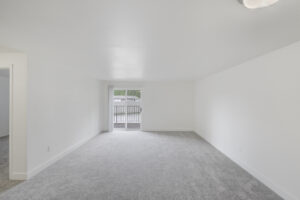 Interior Living Room, White Walls, neutral toned carpeting, glass patio doors, accordion door blinds.