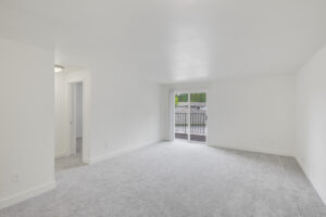 Interior Unit Living Room, White walls, Neutral toned Carpeting, Sliding glass patio doors, accordion door blinds.