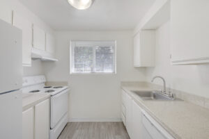 Interior Unit Kitchen, granite like countertops, wood-like floors, white cabinetry, stainless steel sink, window in kitchen.