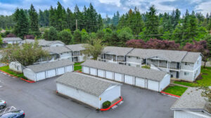 Aerial Exterior of maple crossing, garage parking available, white residential buildings, meticulous landscaping, lush foliage, dense woods in background.